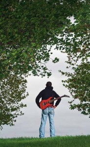 Image of a man with a guitar standing by trees