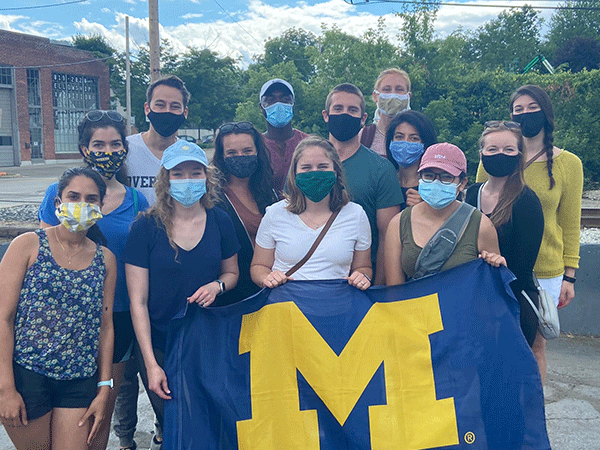 Class of 2023 - 13 resident physicians wearing masks holding a University of Michigan flag