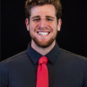 Gabriel Abrams, a young man with facial hair, smiling, wearing a black shirt and red tie. 