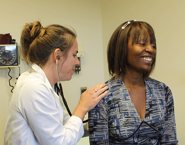 A woman physician listens to a woman's breathing using a stethoscope. 