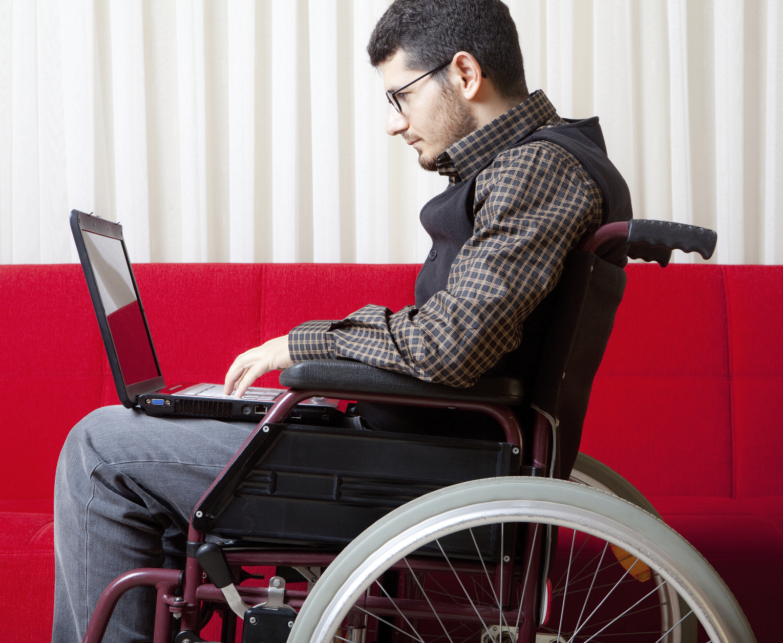 A white man is sitting in a manual wheelchair using a laptop computer 