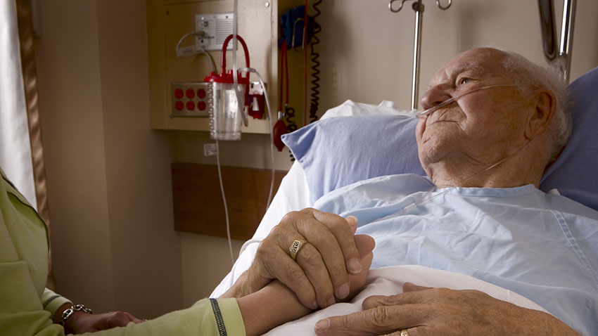 Image of older man in hospital bed holding hand of visitor