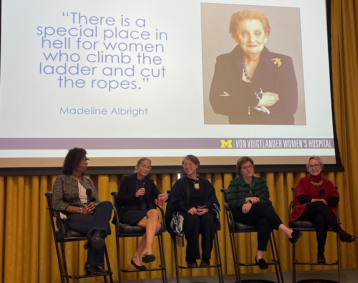 Drs. Erika Newman, Carrie Cunningham, Michelle Caird, Dee Fenner, Diana Farmer talking at the 2023 MWSC Conference with the quote "There is a special place in hell for women who climb the ladder and cut the ropes." by Madeline Albright displayed