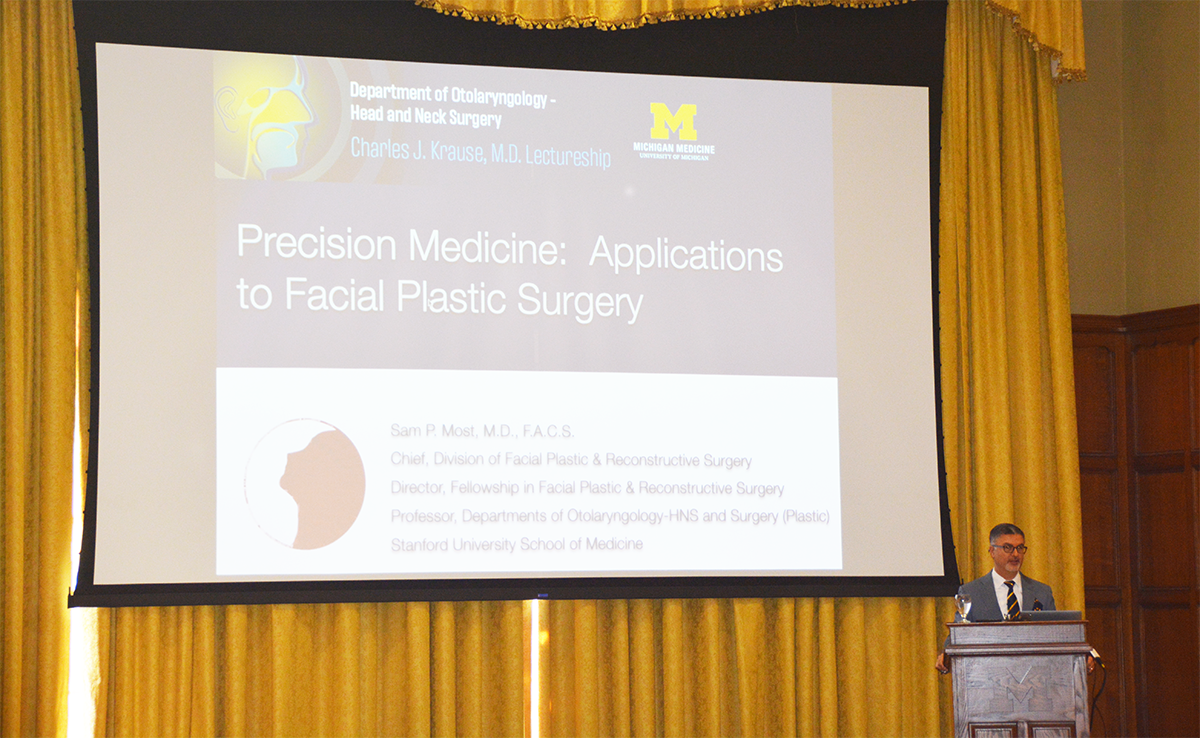 Dr. Sam Most standing at a lectern with his presentation slide up on the projection screen that says "Precision medicine: applications to facial plastic surgery"  