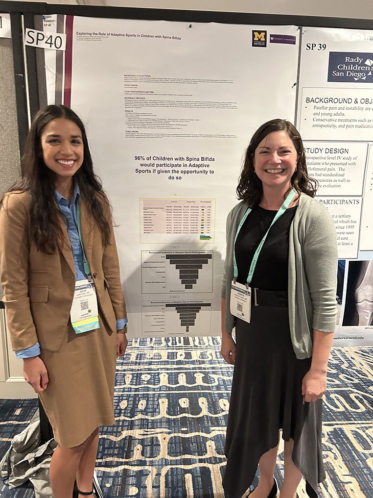 Dr. Jessica Pruente stands with one of our former residents, Julia Shah, in front of their research poster titled "Exploring the Role of Adaptive Sports in Children with Spina Bifida"