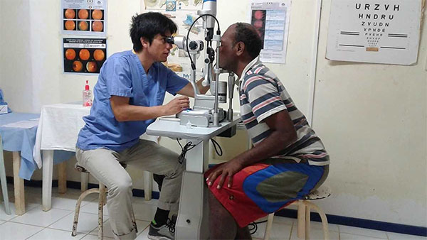 Male medical student in Vanuatu performing an eye exam