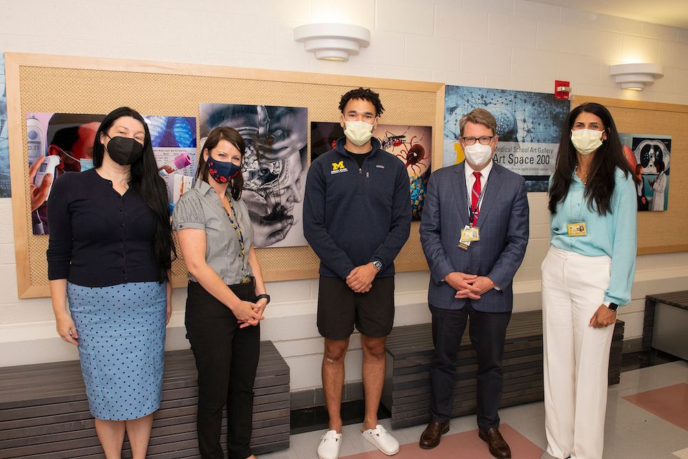 Faculty and staff members pose in front of medical illustrations displayed in a hallway.