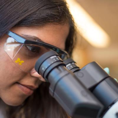 Scientist wearing lab googles looks into a microscope
