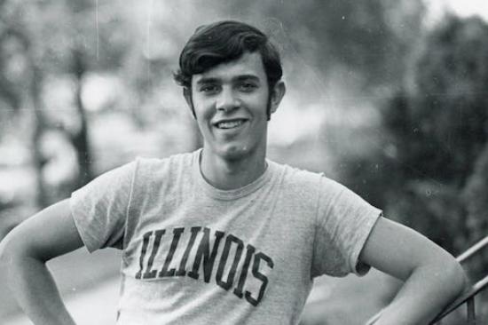 A black and white photo of a teenage Philip Zazove looking at the camera, hand on his hip, wearing a shirt that read Illinois