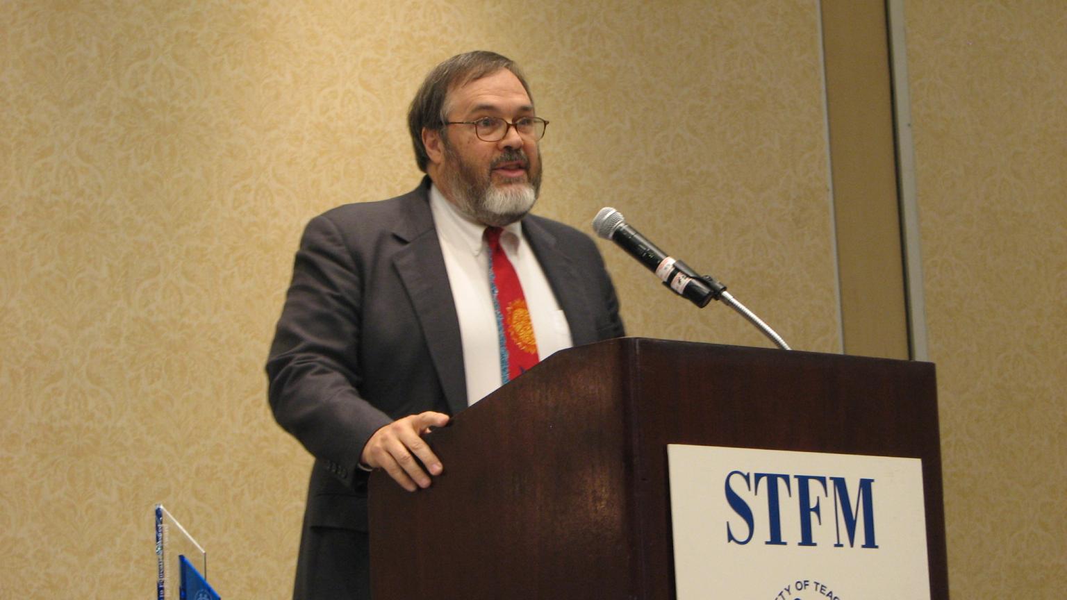 Kent J. Sheets, Ph.D. stands behind a podium that reads STFM