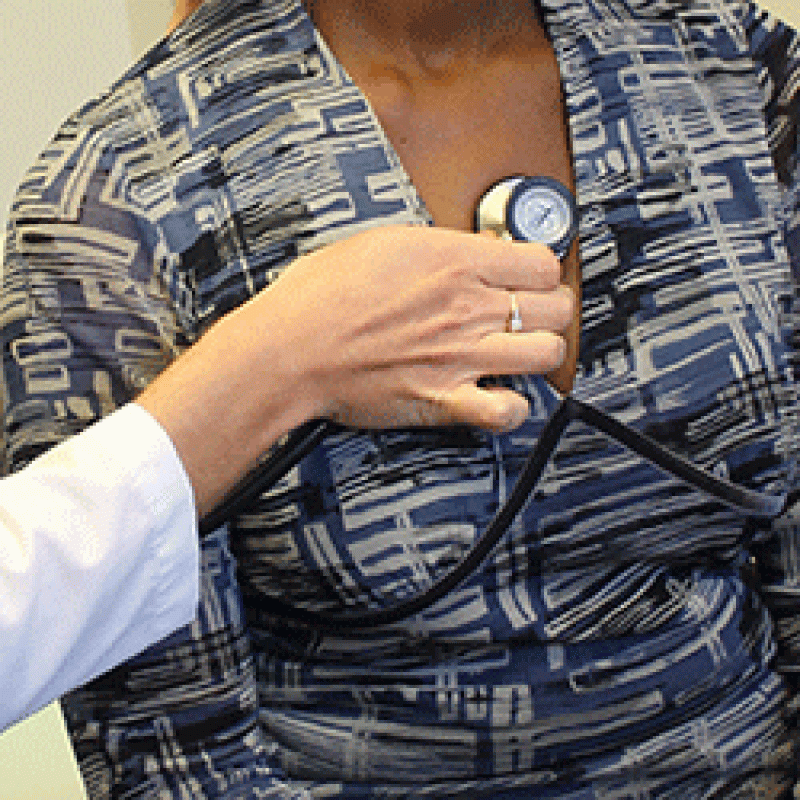 A close up shot of a hand holding a stethoscope to a woman's chest. 