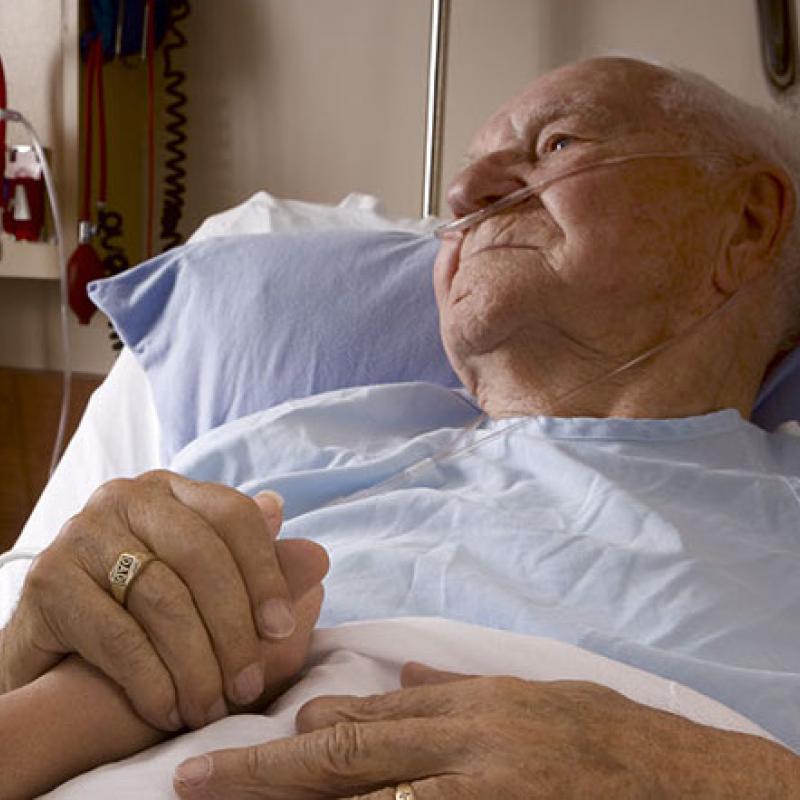 Image of older man in hospital bed holding hand of visitor
