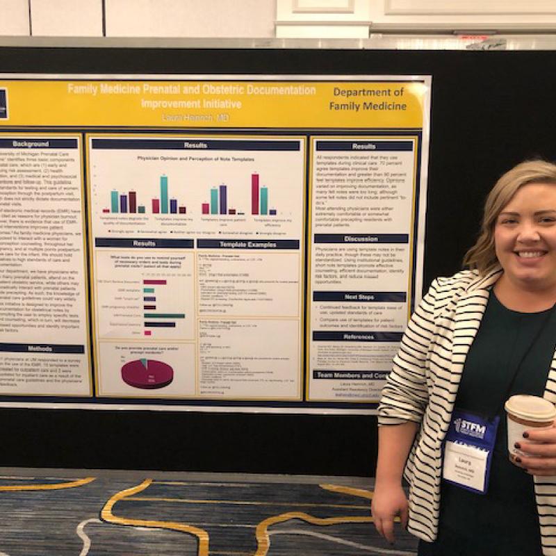 Laura Heinrich stands next to a poster titled Family Medicine Prenatal and Obstetric Documentation Improvement Initiative. 