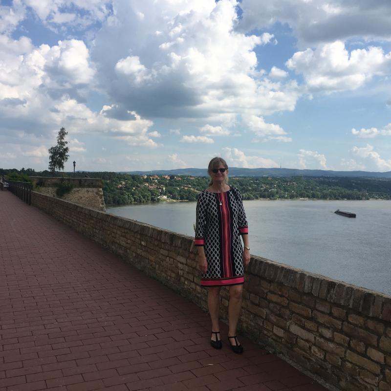 Dr. Djuric stands on a brick path next to a short brick wall. The River Danube is behind her. 