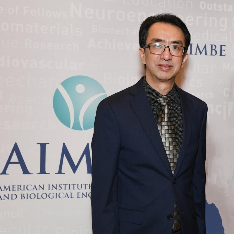 Professor Li stands in front of an AIMBE sign
