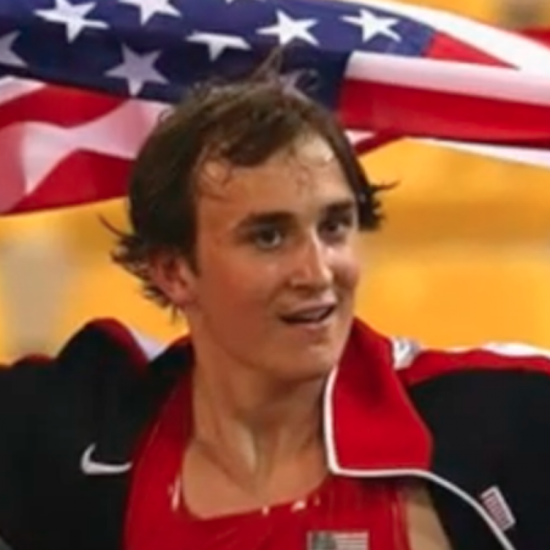 Sam Grewe holds the US flag behind his head and looks away from the camera. 