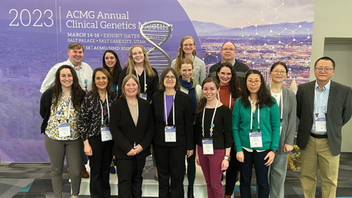 Group of genetics doctors standing and smiling in front of poster boards at a conference.